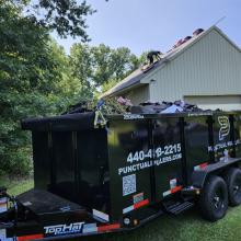 dumpster filled with roofing material and roofers working in background